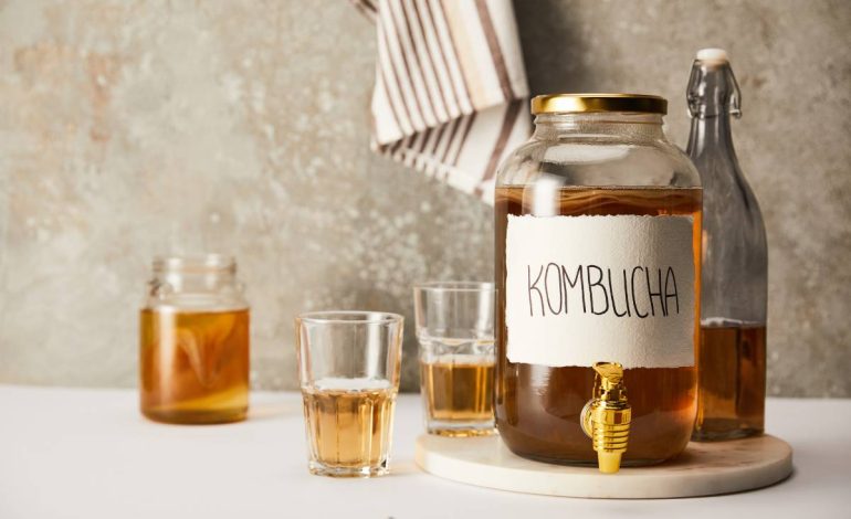 jar with kombucha near glasses and bottle on textured grey background with striped napkin