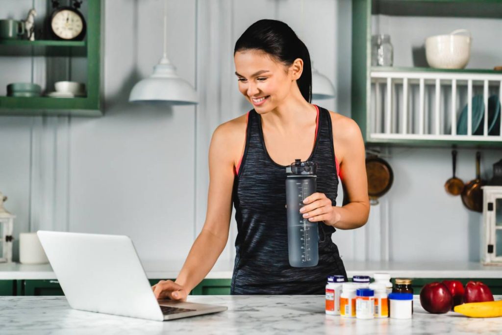 Healthy fit young woman using laptop for additional info about food supplements in the kitchen