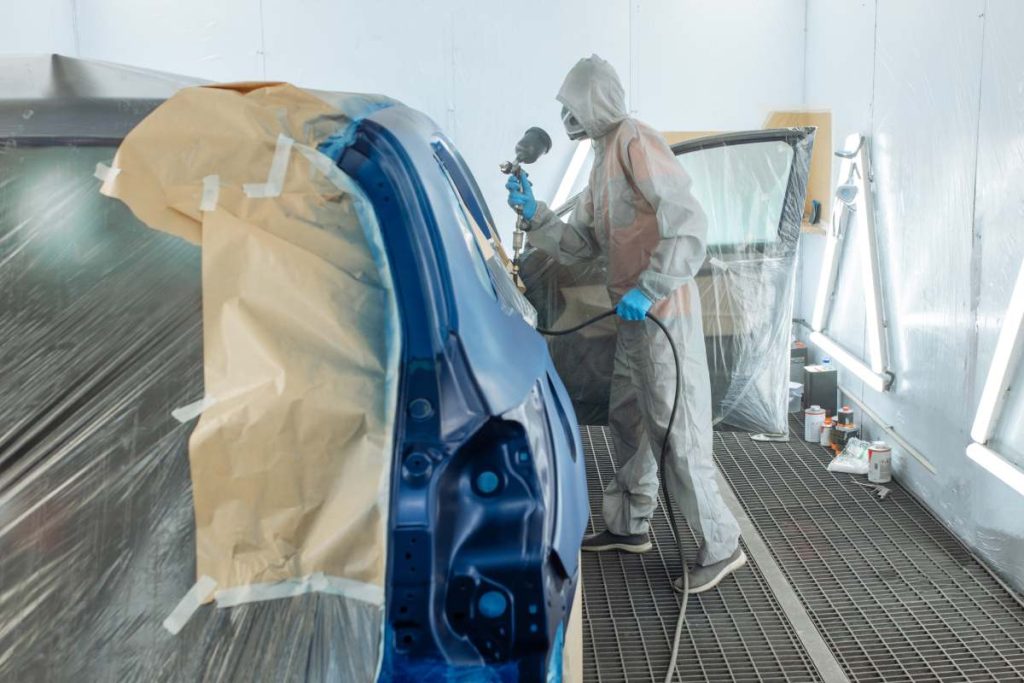 automobile repairman painter hand in protective glove with airbrush pulverizer painting car body in paint chamber