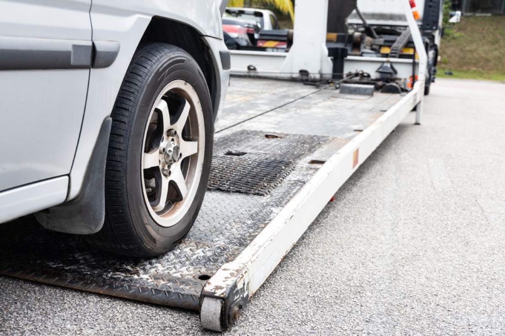 Cable attached to broken down car being pulled onto flatbed tow truck